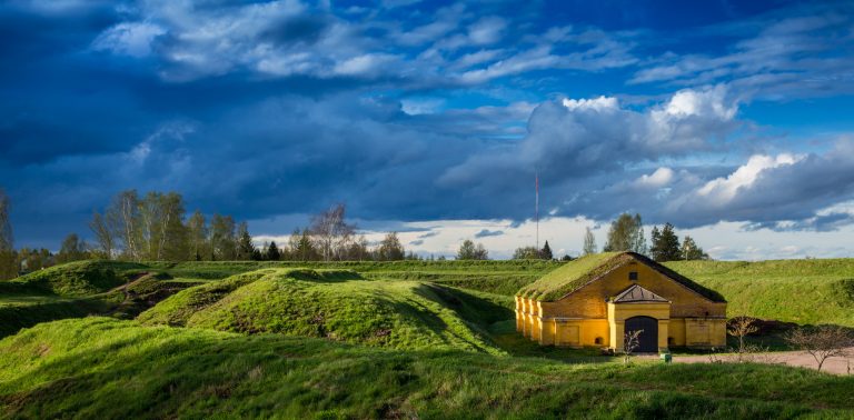 Keltainen rakennus, vihreä linnoitusvalli ja sininen taivas.